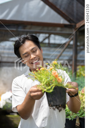 Close up of smiling asian man enjoying time with flowering plant in greenhouse nursery garden center Close up of smiling asian man enjoying time with flowering plant in greenhouse nursery garden center 140841530
