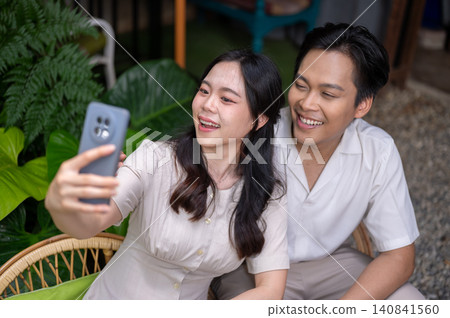 Asian man and woman couple sharing a joyful selfie and enjoying time together in garden at the cafe Asian man and woman couple sharing a joyful selfie and enjoying time together in garden at the cafe 140841560