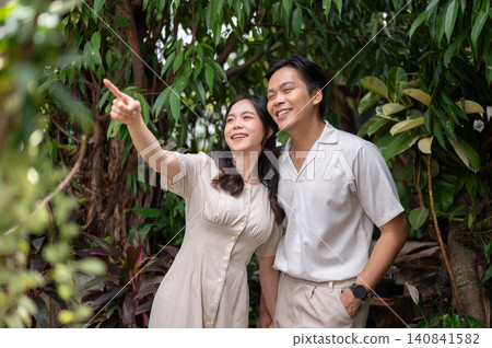 Happy asian man and woman couple pointing toward nature while exploring greenery in tropical garden. 140841582