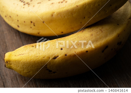 A close-up of a slightly browned banana against a wood grain background. A close-up of a slightly browned banana against a wood grain background. 140841614