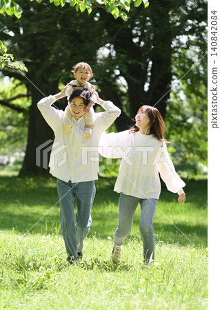 A young family strolling through the park with the daughter on their shoulders. A young family strolling through the park with the daughter on their shoulders. 140842084