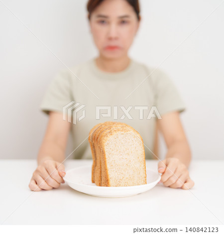 Unhappy woman disgust gesture and Bored to eat bread. concept of gluten intolerance, gluten sensitivity, carb loading concerns, or a disliking for unhealthy dietary habits Unhappy woman disgust gesture and Bored to eat bread. concept of gluten intolerance, gluten sensitivity, carb loading concerns, or a disliking for unhealthy dietary habits 140842123
