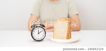 Happy smiling woman with whole wheat bread and alarm clock. concept of intermittent fasting, IF, meal timing, and choosing healthy carbohydrates for a balanced diet and weight loss management Happy smiling woman with whole wheat bread and alarm clock. concept of intermittent fasting, IF, meal timing, and choosing healthy carbohydrates for a balanced diet and weight loss management 140842124