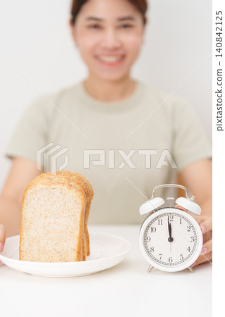 Happy smiling woman with whole wheat bread and alarm clock. concept of intermittent fasting, IF, meal timing, and choosing healthy carbohydrates for a balanced diet and weight loss management Happy smiling woman with whole wheat bread and alarm clock. concept of intermittent fasting, IF, meal timing, and choosing healthy carbohydrates for a balanced diet and weight loss management 140842125