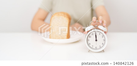 Happy smiling woman with whole wheat bread and alarm clock. concept of intermittent fasting, IF, meal timing, and choosing healthy carbohydrates for a balanced diet and weight loss management Happy smiling woman with whole wheat bread and alarm clock. concept of intermittent fasting, IF, meal timing, and choosing healthy carbohydrates for a balanced diet and weight loss management 140842126