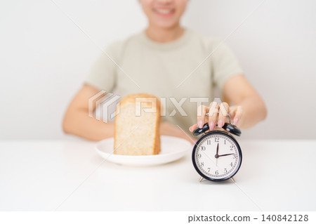 Happy smiling woman with whole wheat bread and alarm clock. concept of intermittent fasting, IF, meal timing, and choosing healthy carbohydrates for a balanced diet and weight loss management Happy smiling woman with whole wheat bread and alarm clock. concept of intermittent fasting, IF, meal timing, and choosing healthy carbohydrates for a balanced diet and weight loss management 140842128