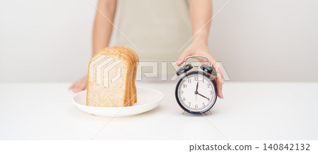 Happy smiling woman with whole wheat bread and alarm clock. concept of intermittent fasting, IF, meal timing, and choosing healthy carbohydrates for a balanced diet and weight loss management Happy smiling woman with whole wheat bread and alarm clock. concept of intermittent fasting, IF, meal timing, and choosing healthy carbohydrates for a balanced diet and weight loss management 140842132