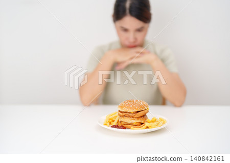 Unhappy woman disgust gesture and Bored to eat Juicy beef burger and potato chips. Unhealthy, High calorie, Fast food craving, Obesity, diet, weight loss and junk food 140842161