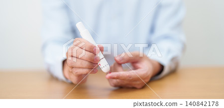Hand using lancet pen on finger with Blood drop glucose testing or Diabetes checking by digital blood glucose meter. blood sugar level, Diabetes Day, Glycemia, Hypoglycemia, Hyperglycemia and insulin 140842178