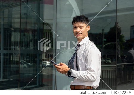 Asian businessman office worker using smartphone while walking near modern glass facade of building. Asian businessman office worker using smartphone while walking near modern glass facade of building. 140842269