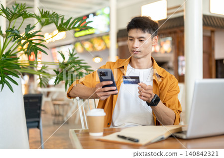 Asian man customer holding smartphone and credit card while making secure online payment in the cafe Asian man customer holding smartphone and credit card while making secure online payment in the cafe 140842321