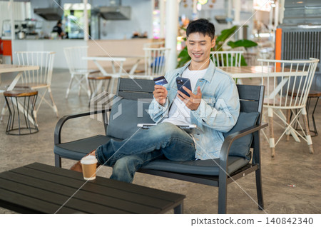 Asian man customer sitting in cafe using smartphone and credit card for online shopping or payment. Asian man customer sitting in cafe using smartphone and credit card for online shopping or payment. 140842340