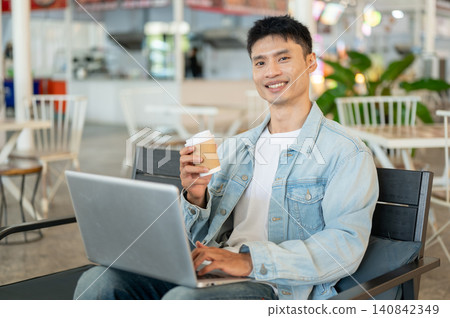 Asian man freelancer enjoy drinking coffee while working on laptop sitting in modern cafe workspace. Asian man freelancer enjoy drinking coffee while working on laptop sitting in modern cafe workspace. 140842349
