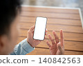 Close up of white screen smartphone held in man's hand and shallow depth background at table in cafe 140842563