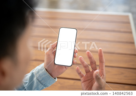 Close up of white screen smartphone held in man's hand and shallow depth background at table in cafe Close up of white screen smartphone held in man's hand and shallow depth background at table in cafe 140842563