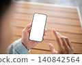 Close up of white screen smartphone in hand over wooden table, ideal for app presentation and design 140842564