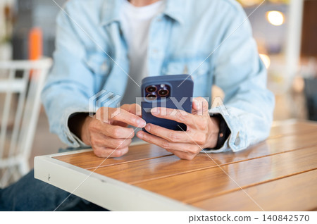 Close up of a man's hands using smartphone at cafe table, browsing online content in relaxed setting Close up of a man's hands using smartphone at cafe table, browsing online content in relaxed setting 140842570