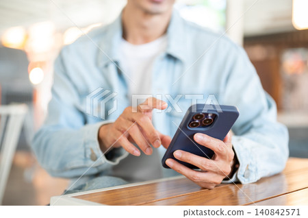 Close up of man's hand interacting with smartphone sitting at cafe table showcasing digital lifestyle 140842571