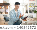 Asian man using a smartphone in cafe environment, enjoying mobile communication and online services. 140842572