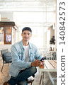 Asian man customer in denim and jeans sitting at table in cafe with smartphone showcasing lifestyle. 140842573
