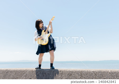 一位高中女生在沙灘上彈奏電吉他。 一位高中女生在沙灘上彈奏電吉他。 140842841