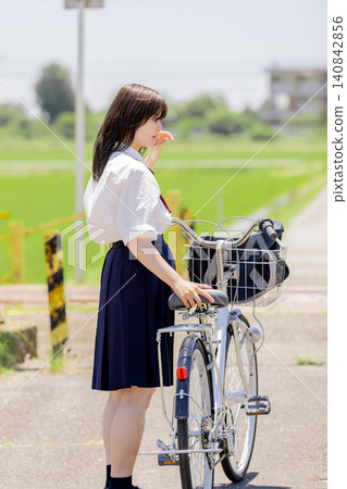 A high school girl is lost in thought while pushing her bicycle through a rural landscape. A high school girl is lost in thought while pushing her bicycle through a rural landscape. 140842856