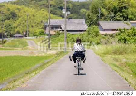 一位高中女生騎著腳踏車沿著鄉村小路回家,這是她的背影。 一位高中女生騎著腳踏車沿著鄉村小路回家,這是她的背影。 140842869