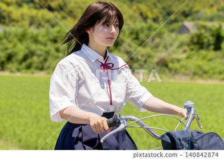 A smiling high school girl rides her bicycle along a rural route to school. A smiling high school girl rides her bicycle along a rural route to school. 140842874