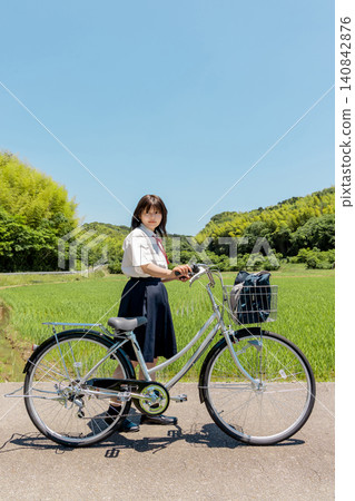 A high school girl on her bicycle, on her way to school, in a rural landscape. A high school girl on her bicycle, on her way to school, in a rural landscape. 140842876