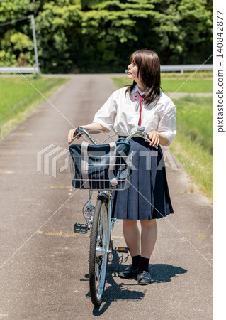 A high school girl looks up at the sky while pushing her bicycle along a rural route to school. A high school girl looks up at the sky while pushing her bicycle along a rural route to school. 140842877