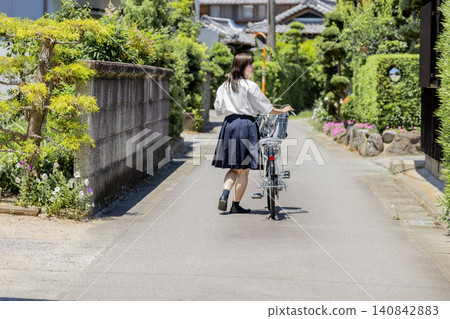 一位高中女生推著自行車,沿著鄉村住宅區的學校小路行走,這是她的背影。 一位高中女生推著自行車,沿著鄉村住宅區的學校小路行走,這是她的背影。 140842883