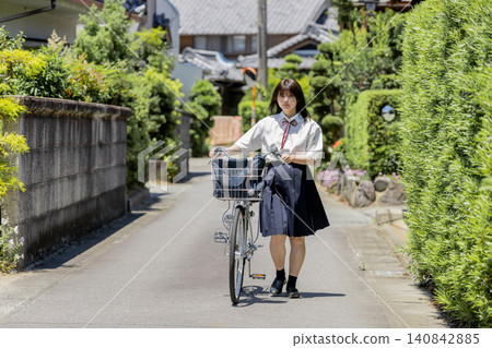 一名高中女生推著自行車，沿著鄉村住宅區的學校路線行走。 140842885