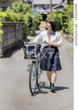 A high school girl walks along a school route in a rural residential area, pushing her bicycle. A high school girl walks along a school route in a rural residential area, pushing her bicycle. 140842886