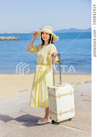A young woman in a straw hat carrying a suitcase at a seaside resort. A young woman in a straw hat carrying a suitcase at a seaside resort. 140842914