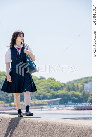 A high school girl walking along a breakwater by the sea under a summer blue sky. A high school girl walking along a breakwater by the sea under a summer blue sky. 140843014