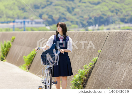 A portrait of a high school girl pushing her bicycle on a seaside school route. A portrait of a high school girl pushing her bicycle on a seaside school route. 140843059