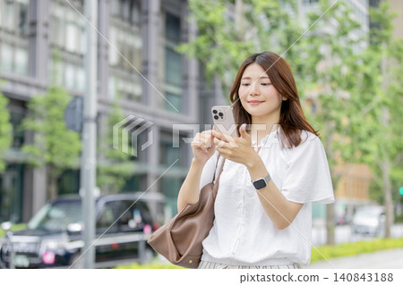 一位微笑的日本女性在辦公區使用智慧型手機。 140843188