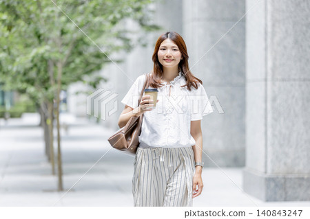 一位日本女性正在享受悠閒的時光,她手裡拿著一杯外帶咖啡。 一位日本女性正在享受悠閒的時光,她手裡拿著一杯外帶咖啡。 140843247