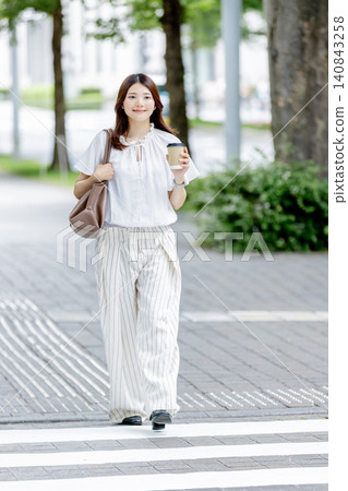 一位日本女子手持一杯咖啡,走過辦公區。 一位日本女子手持一杯咖啡,走過辦公區。 140843258
