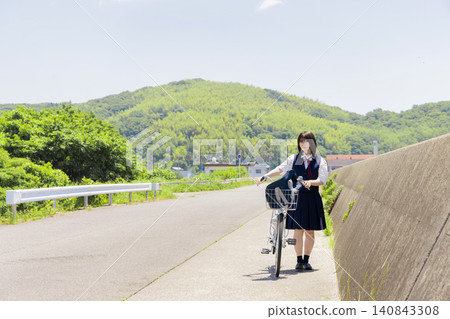 一名高中女生推著腳踏車走在海邊的上學路上。 一名高中女生推著腳踏車走在海邊的上學路上。 140843308