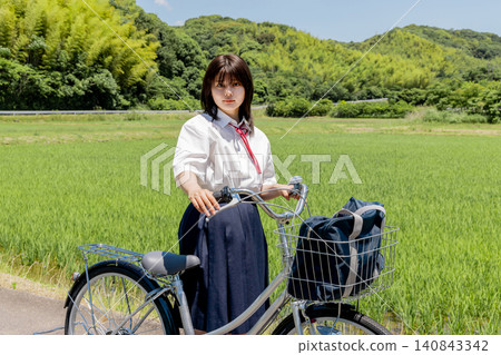 Portrait of a high school girl cycling to school amidst a rural landscape. 140843342