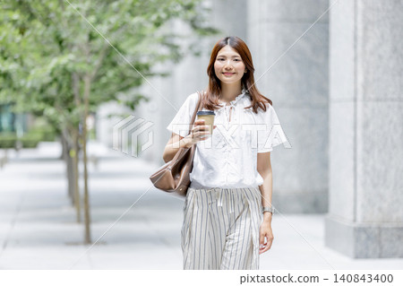 一位日本女性正在享受悠閒的時光,她手裡拿著一杯外帶咖啡。 一位日本女性正在享受悠閒的時光,她手裡拿著一杯外帶咖啡。 140843400