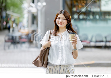 一位日本女子手持一杯外帶咖啡走在城市裡。 一位日本女子手持一杯外帶咖啡走在城市裡。 140843405