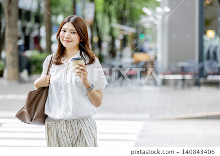 一位日本女子手持一杯外帶咖啡走在城市裡。 一位日本女子手持一杯外帶咖啡走在城市裡。 140843406