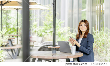 A businesswoman using her smartphone and laptop on a terrace. 140843443