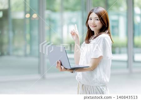 A Japanese woman pointing while holding a laptop. A Japanese woman pointing while holding a laptop. 140843513