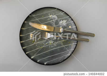 Dirty plate with fork and knife lies after meal on table. Used dish shows food leftovers and dining process end. Concept reflects eating, kitchen routine, daily life activity.. Dirty plate with fork and knife lies after meal on table. Used dish shows food leftovers and dining process end. Concept reflects eating, kitchen routine, daily life activity.. 140844002