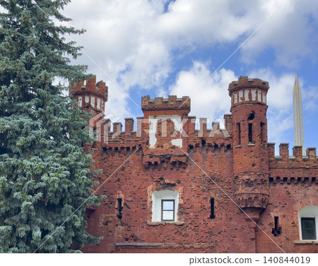 Red brick fortress tower rises near trees against sky. Historic architecture stands tall with strong walls and details. Cultural landmark concept reflects history, heritage, travel Red brick fortress tower rises near trees against sky. Historic architecture stands tall with strong walls and details. Cultural landmark concept reflects history, heritage, travel 140844019