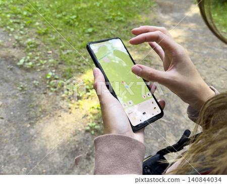 Hands use smartphone map application in outdoor setting. Person navigates forest using digital interface on screen. Technology concept reflects navigation, travel, location, mobile Hands use smartphone map application in outdoor setting. Person navigates forest using digital interface on screen. Technology concept reflects navigation, travel, location, mobile 140844034