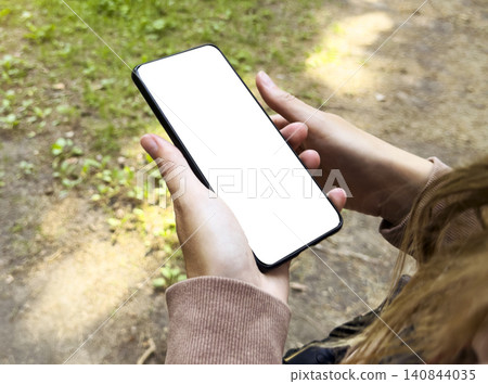 Hands hold smartphone with blank screen in outdoor setting. Mobile device displays empty mock up space for inserting content. Technology concept reflects communication, interface, Hands hold smartphone with blank screen in outdoor setting. Mobile device displays empty mock up space for inserting content. Technology concept reflects communication, interface, 140844035